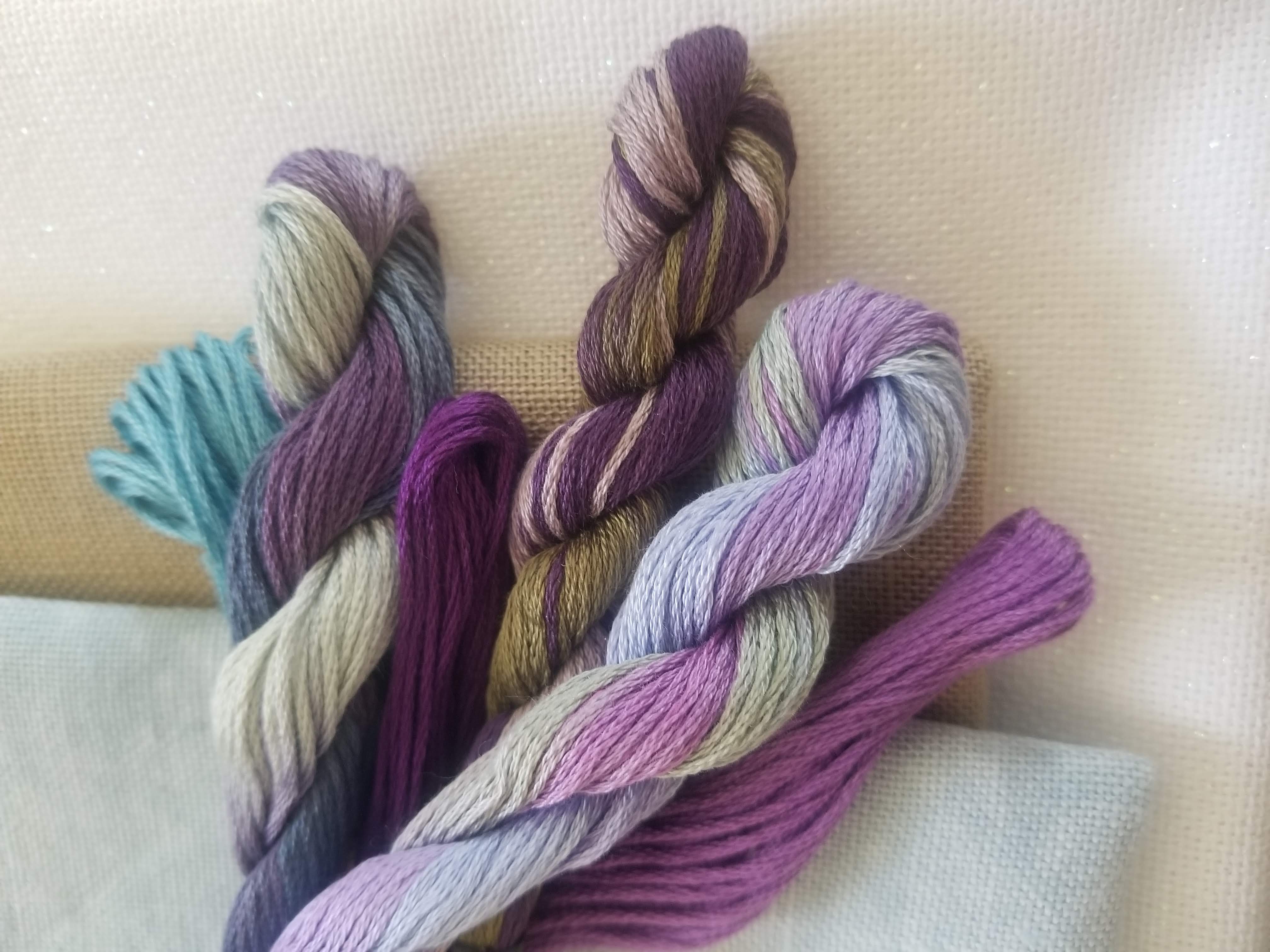 A bundle of cross-stitch floss in purples, sage, and warm grays